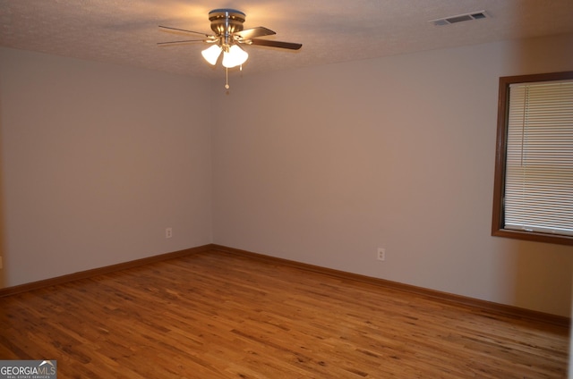 spare room featuring baseboards, a textured ceiling, visible vents, and wood finished floors