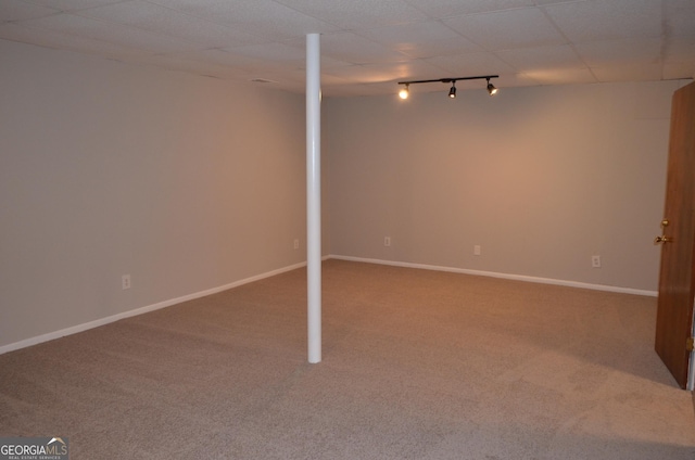 finished below grade area featuring a paneled ceiling, carpet, rail lighting, and baseboards