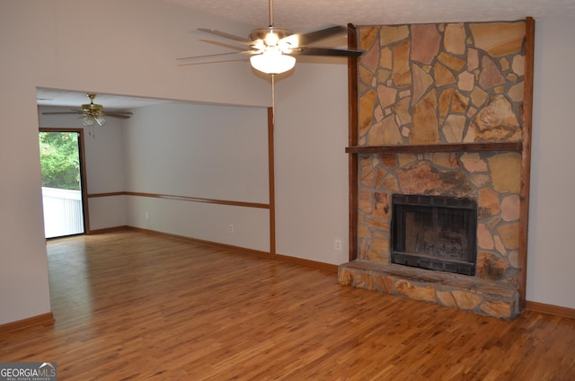 unfurnished living room featuring a textured ceiling, ceiling fan, a fireplace, wood finished floors, and baseboards