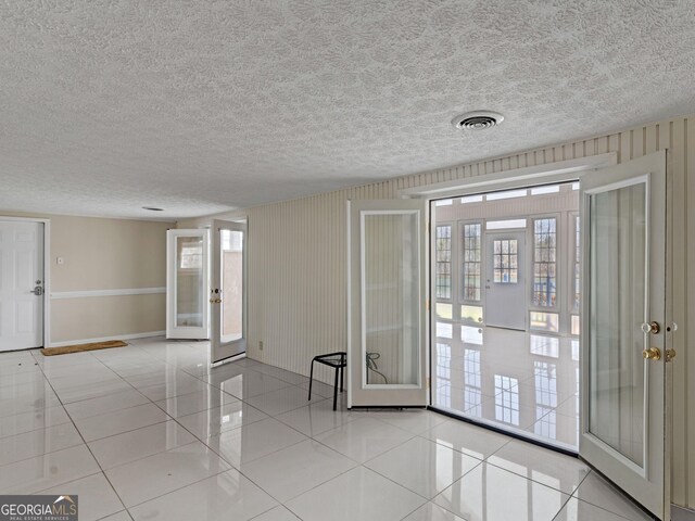 unfurnished room featuring a textured ceiling, light tile patterned flooring, visible vents, baseboards, and french doors