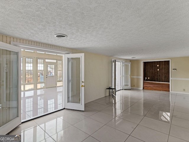 unfurnished room with a textured ceiling, french doors, visible vents, and tile patterned floors