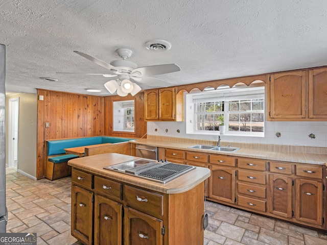 kitchen featuring visible vents, brown cabinetry, light countertops, stone tile flooring, and a sink