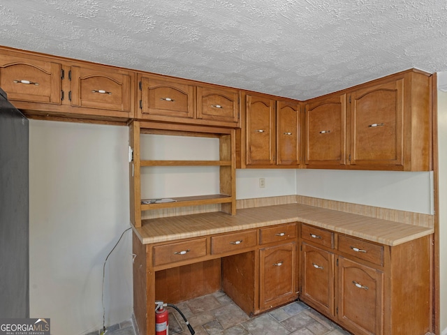 kitchen featuring a textured ceiling, open shelves, brown cabinetry, and light countertops