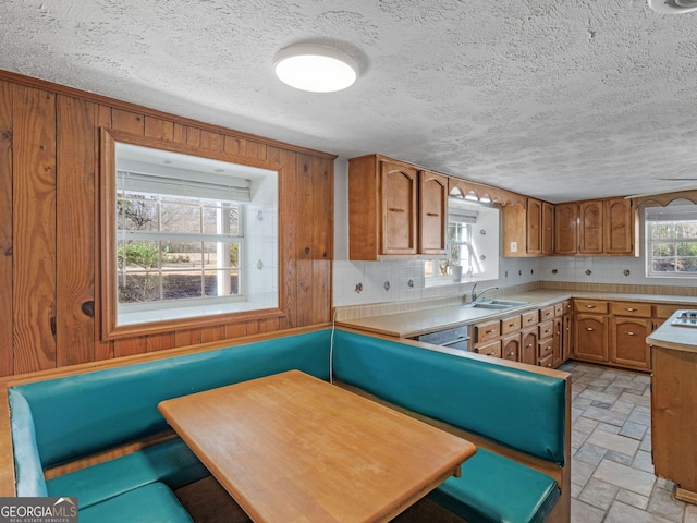 kitchen featuring brown cabinets, stone tile floors, light countertops, wood walls, and dishwasher