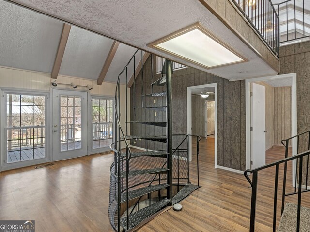 stairway featuring a textured ceiling, high vaulted ceiling, wood finished floors, visible vents, and beam ceiling