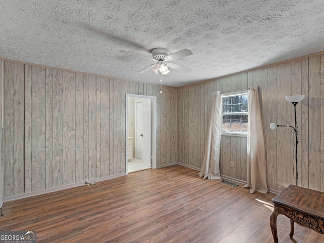 empty room with baseboards, visible vents, ceiling fan, wood finished floors, and a textured ceiling