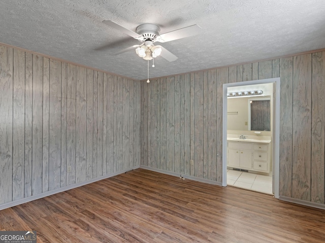 empty room with baseboards, ceiling fan, wood finished floors, a textured ceiling, and a sink