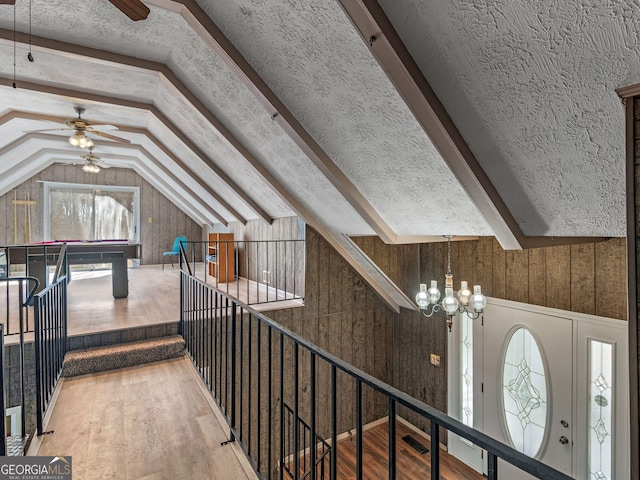 interior space with wooden walls, wood finished floors, vaulted ceiling with beams, a textured ceiling, and ceiling fan with notable chandelier