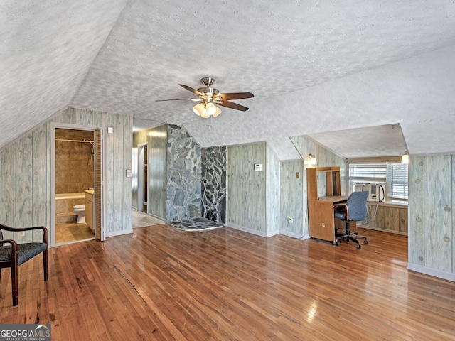 additional living space with lofted ceiling, wooden walls, a textured ceiling, and hardwood / wood-style floors