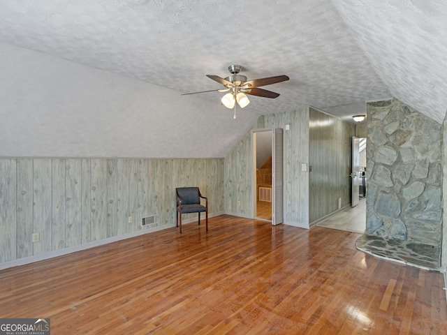 additional living space with lofted ceiling, a textured ceiling, visible vents, and hardwood / wood-style floors