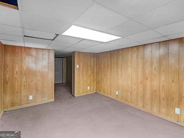 finished basement featuring a paneled ceiling, wood walls, and baseboards