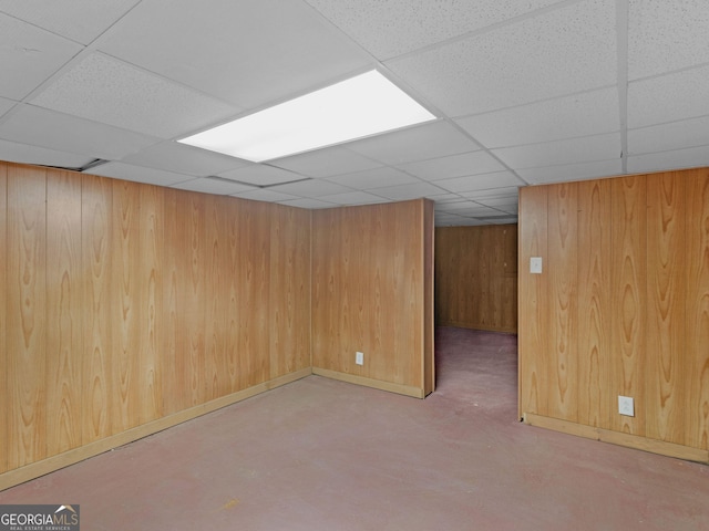 finished basement with wood walls, a drop ceiling, and baseboards