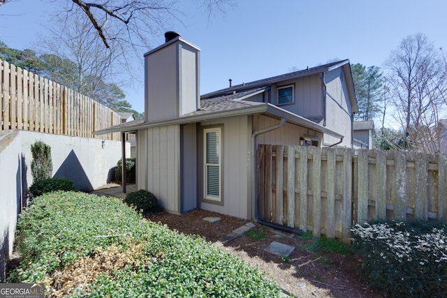 back of property featuring a shingled roof, a chimney, and fence