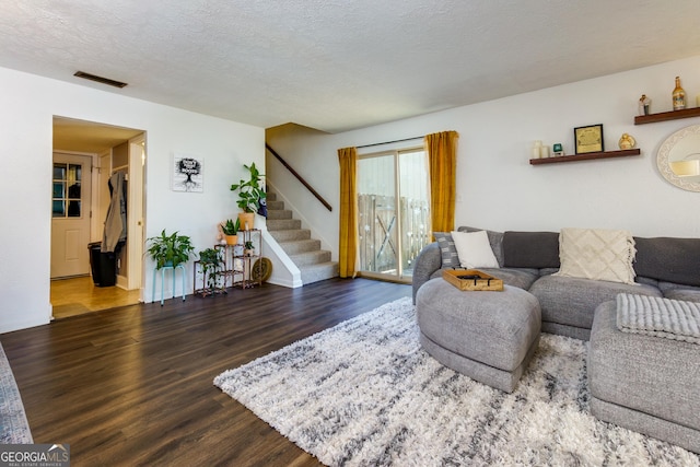 living area featuring stairway, a textured ceiling, visible vents, and wood finished floors