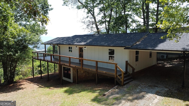 rear view of house featuring a shingled roof, dirt driveway, a carport, and a wooden deck