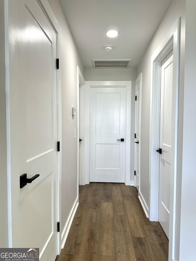 corridor with baseboards, visible vents, and dark wood-type flooring