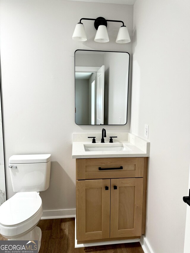 bathroom with toilet, baseboards, wood finished floors, and vanity