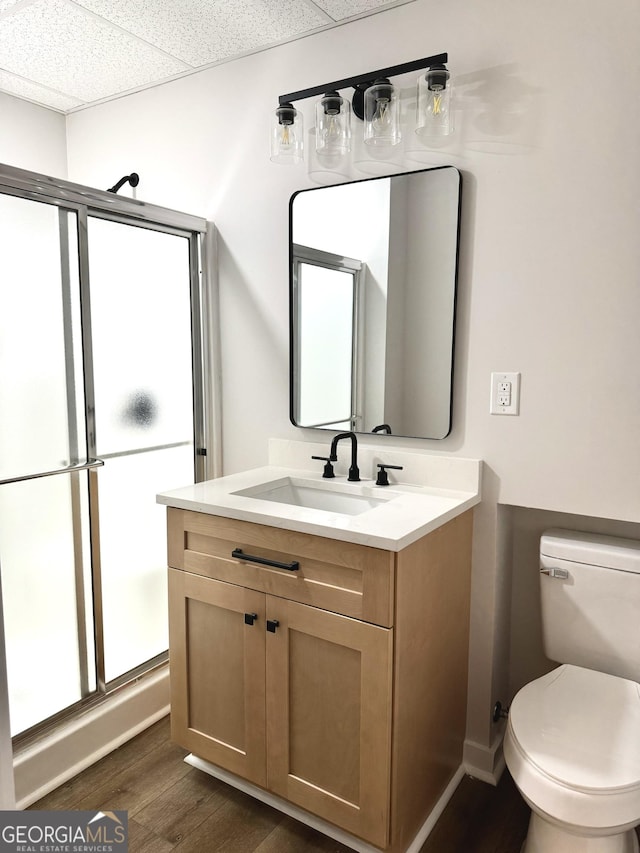 full bath with a stall shower, a drop ceiling, toilet, wood finished floors, and vanity