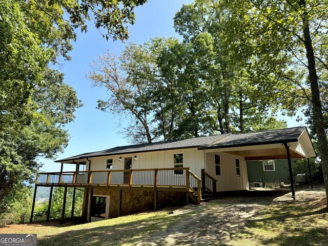 rear view of house with an attached carport, a wooden deck, and dirt driveway