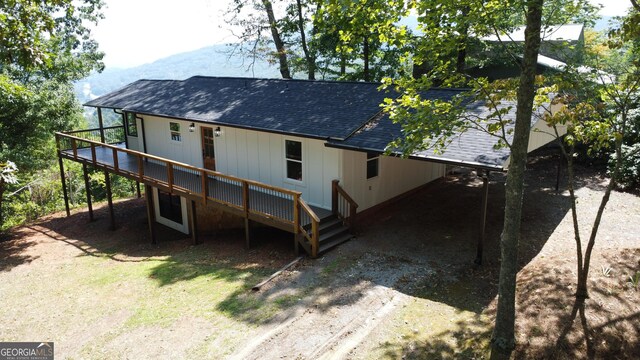 back of property featuring dirt driveway, roof with shingles, and a wooden deck