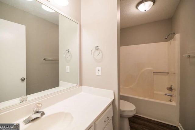 bathroom with toilet, wood finished floors, a textured ceiling, vanity, and washtub / shower combination