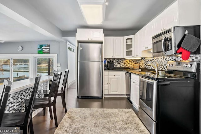 kitchen featuring tasteful backsplash, appliances with stainless steel finishes, glass insert cabinets, white cabinetry, and a sink