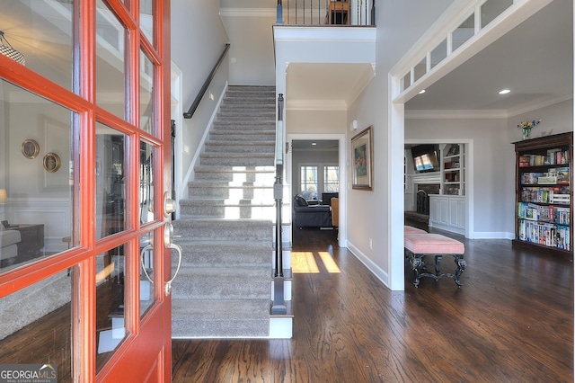 foyer entrance with a fireplace, crown molding, stairway, wood finished floors, and baseboards