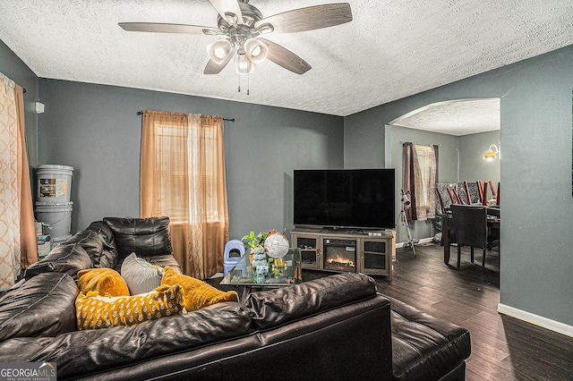 living room featuring a textured ceiling, arched walkways, wood finished floors, a ceiling fan, and baseboards