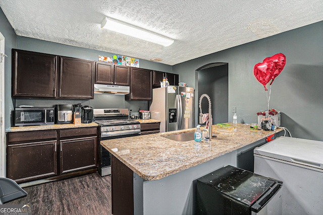 kitchen with under cabinet range hood, a sink, dark brown cabinets, appliances with stainless steel finishes, and dark wood finished floors