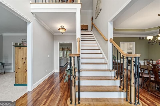 staircase with baseboards, ornamental molding, visible vents, and an inviting chandelier