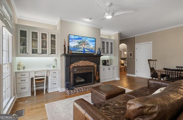 living room with visible vents, a brick fireplace, wood finished floors, arched walkways, and a ceiling fan