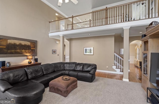 living area featuring ornamental molding, ceiling fan, arched walkways, a towering ceiling, and stairs