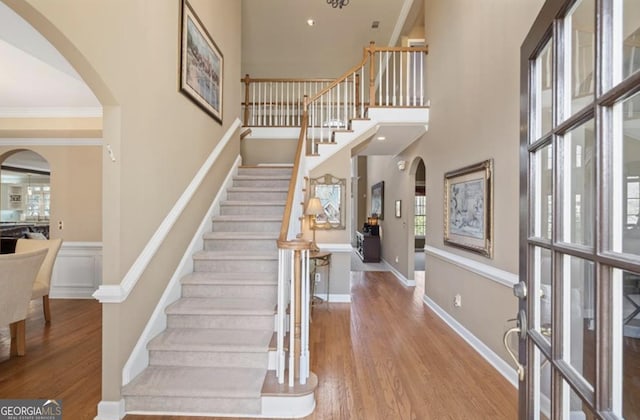 entrance foyer with arched walkways, stairs, baseboards, and wood finished floors