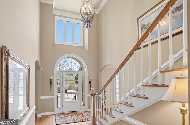 foyer with a notable chandelier, wood finished floors, arched walkways, baseboards, and stairs