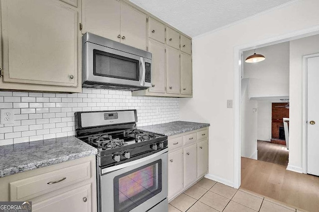 kitchen featuring stainless steel appliances, decorative backsplash, light tile patterned flooring, a textured ceiling, and baseboards