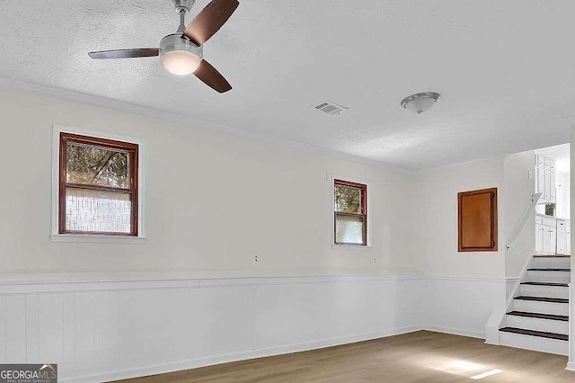 spare room with a healthy amount of sunlight, stairs, visible vents, and wood finished floors