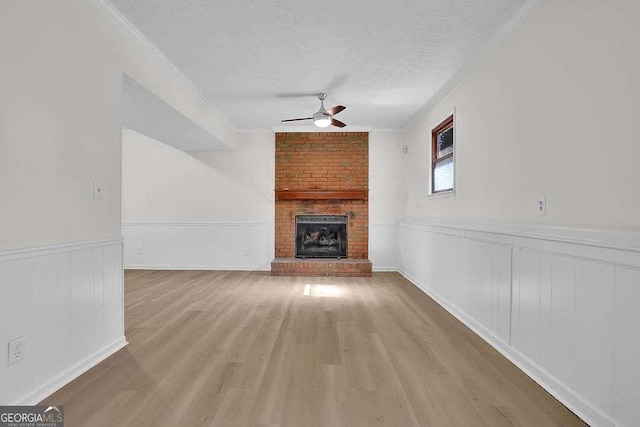 unfurnished living room featuring a wainscoted wall, ceiling fan, wood finished floors, a textured ceiling, and a brick fireplace