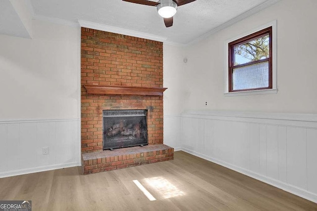 unfurnished living room with wainscoting, a fireplace, wood finished floors, and crown molding