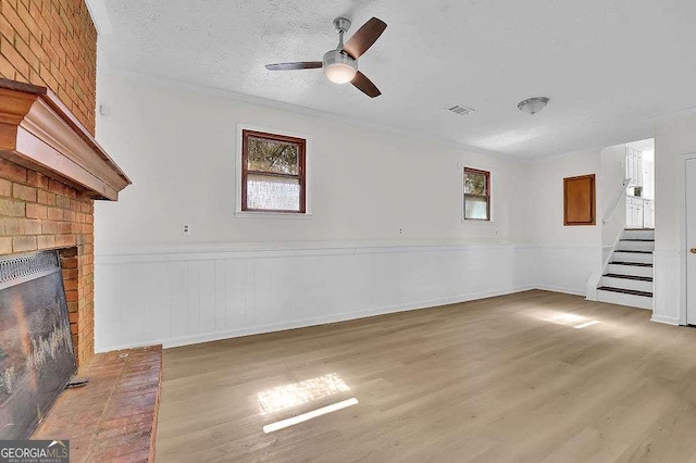 unfurnished living room featuring a textured ceiling, wood finished floors, visible vents, stairs, and a brick fireplace