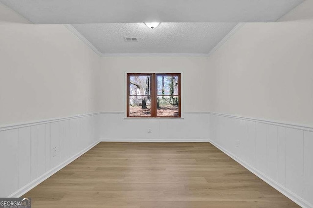 unfurnished room with wainscoting, crown molding, a textured ceiling, and wood finished floors