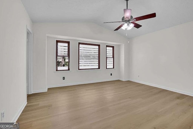 spare room with vaulted ceiling, baseboards, a ceiling fan, and light wood-style floors