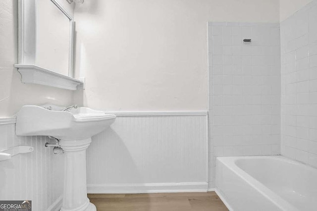 bathroom with a wainscoted wall, bathtub / shower combination, and wood finished floors