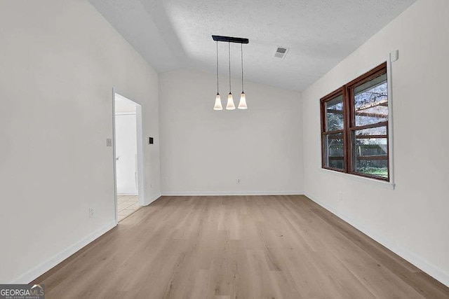 unfurnished dining area featuring lofted ceiling, a textured ceiling, visible vents, and light wood-style floors