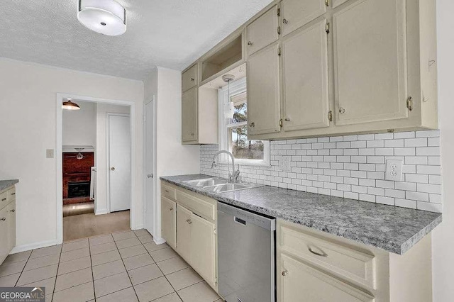 kitchen with light tile patterned floors, decorative backsplash, stainless steel dishwasher, a sink, and a textured ceiling