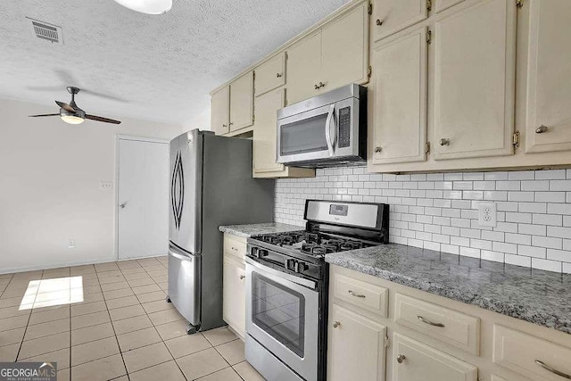 kitchen with light tile patterned floors, stainless steel appliances, decorative backsplash, cream cabinets, and a ceiling fan