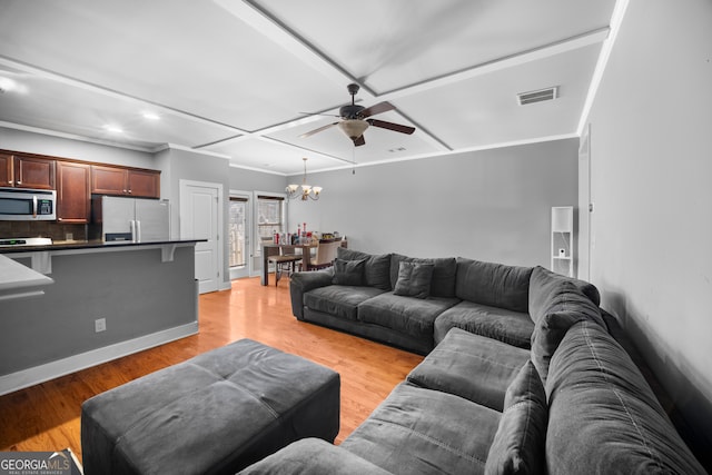 living area featuring light wood finished floors, visible vents, baseboards, ornamental molding, and ceiling fan with notable chandelier