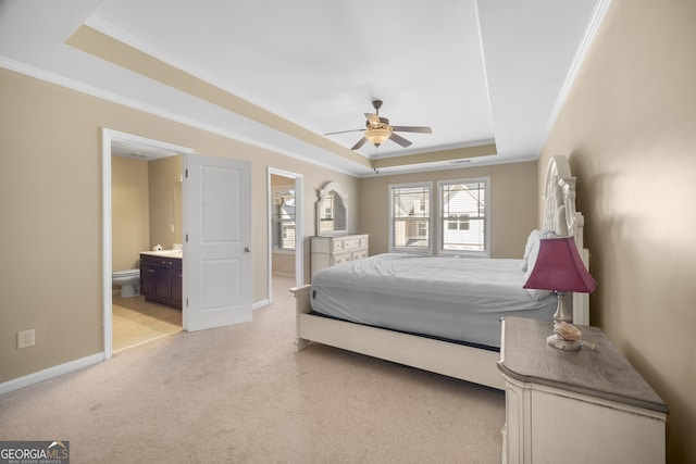 bedroom with connected bathroom, light colored carpet, baseboards, a raised ceiling, and crown molding