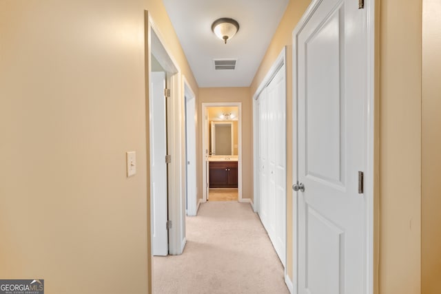 hallway featuring baseboards, visible vents, and light colored carpet