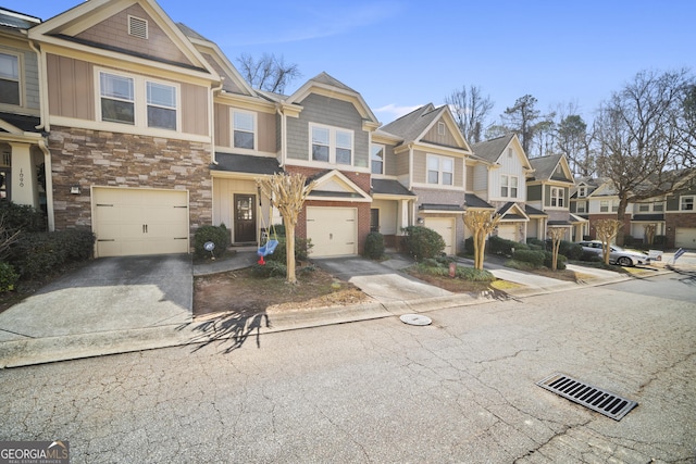 townhome / multi-family property with a garage, stone siding, a residential view, and concrete driveway