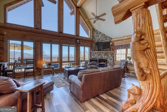 living room with rustic walls, a ceiling fan, a stone fireplace, light wood-type flooring, and a mountain view